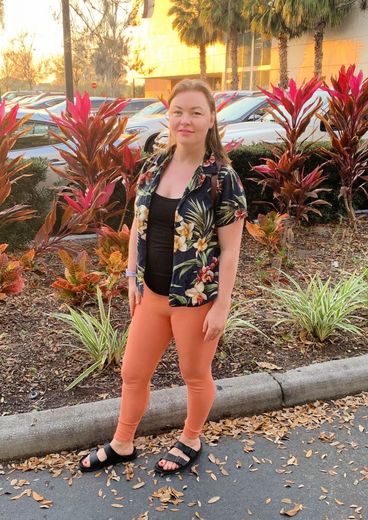 Florida fashion. Woman in front of tropical plants wearing a Hawaiian shirt and orange pants.